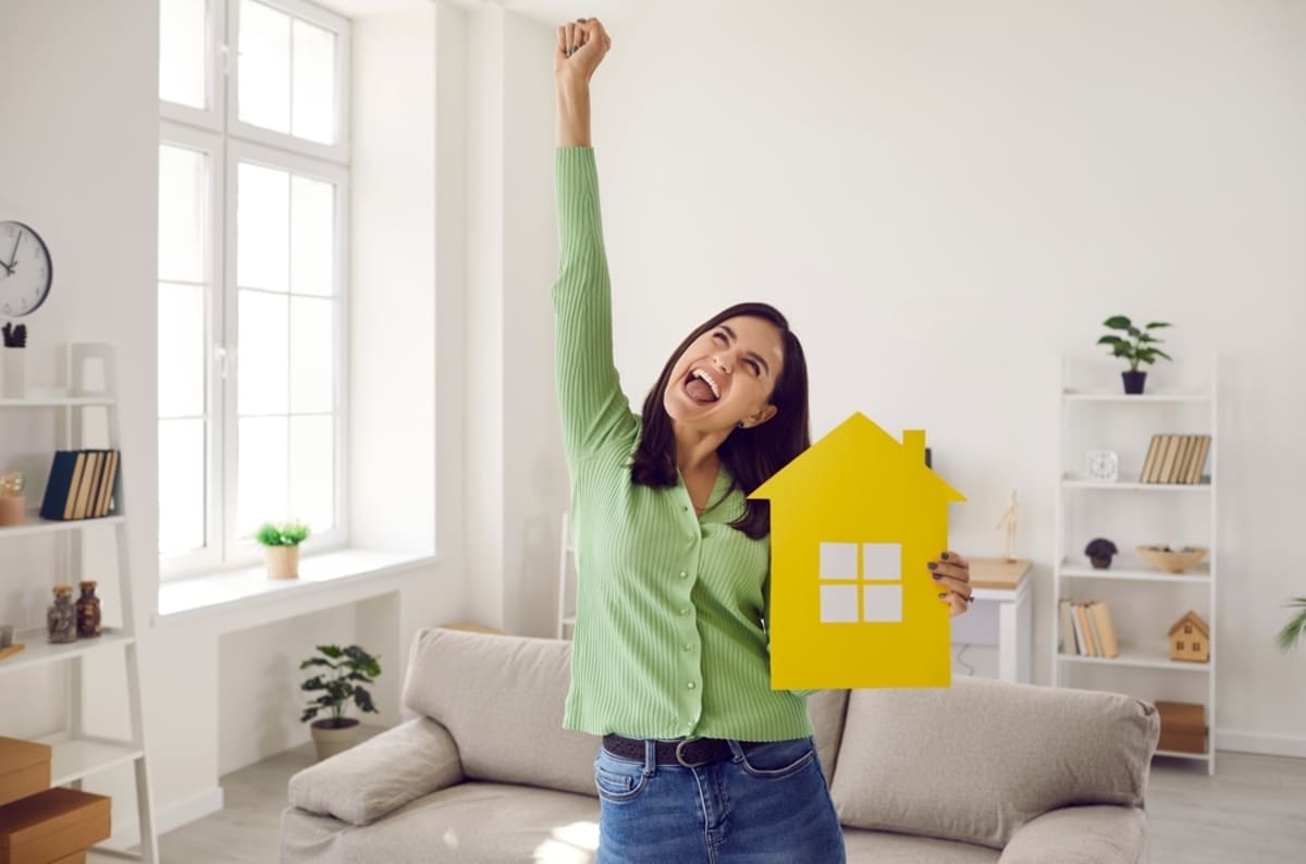A happy woman cheering and holding a yellow house