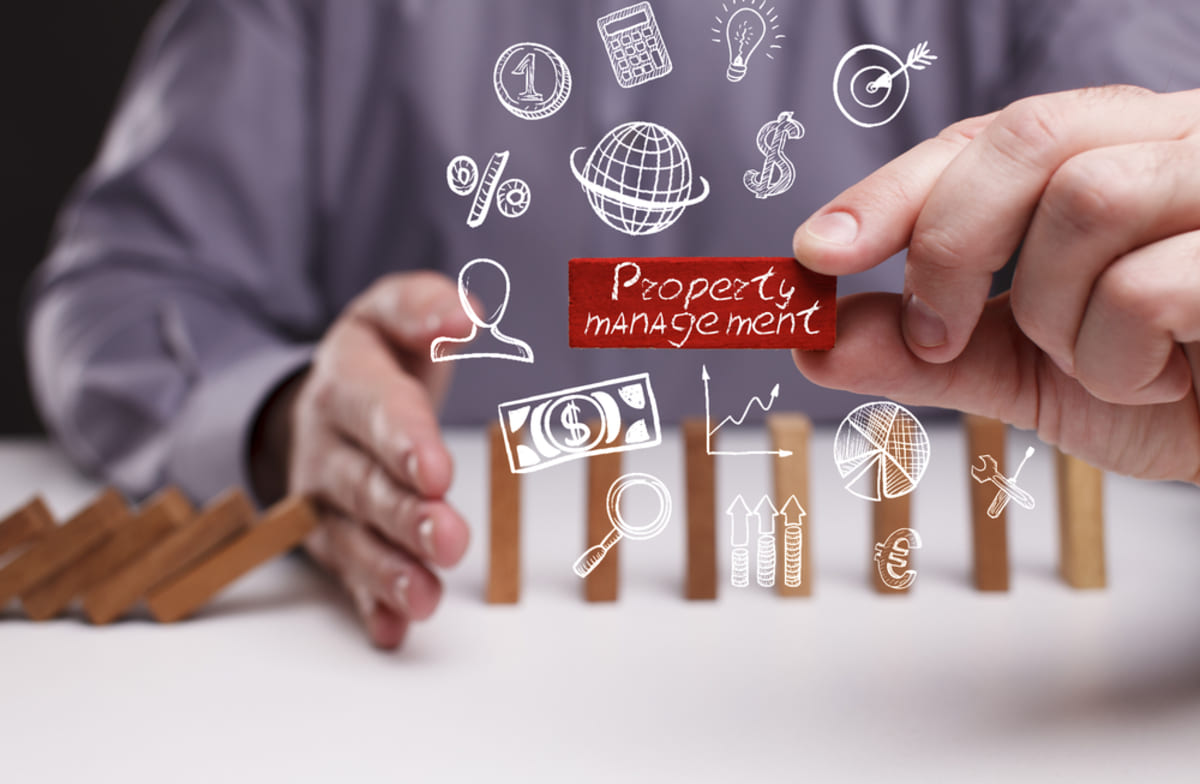 A man holds a small wooden block showing the word "property management," working with a property management company concept.