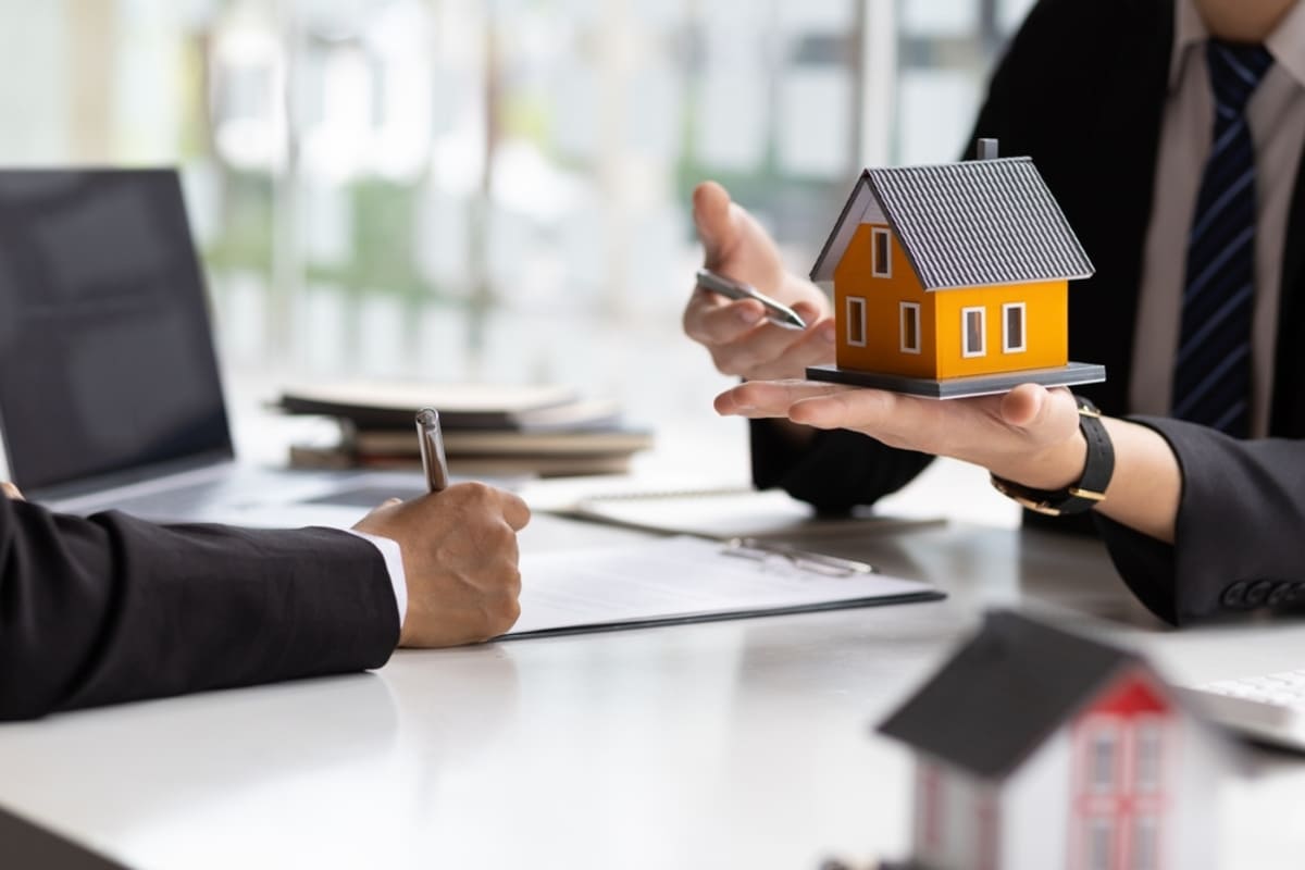 A person pointing to a small house with a pen and another person writing, property management Indianapolis concept