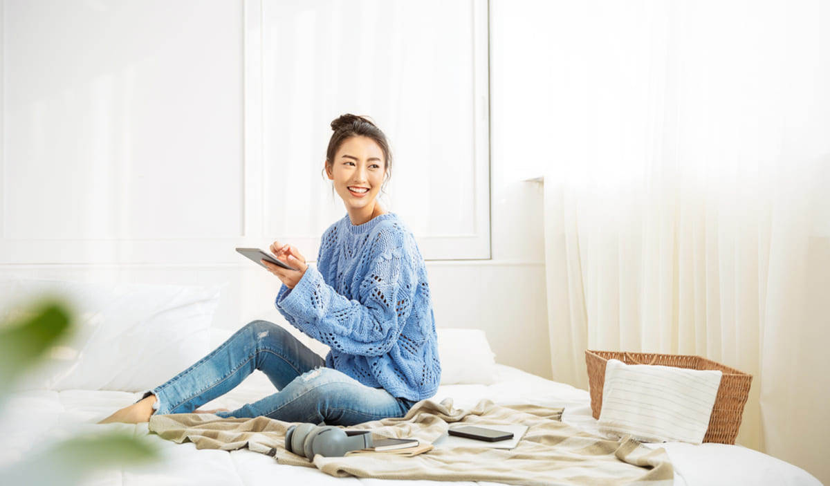 A person sitting on a bed smiling and holding a tablet - property management Indianapolis concept