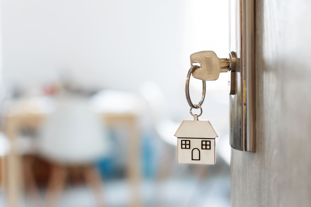 A key with a small house on the keychain in a keyhole, property management company concept.