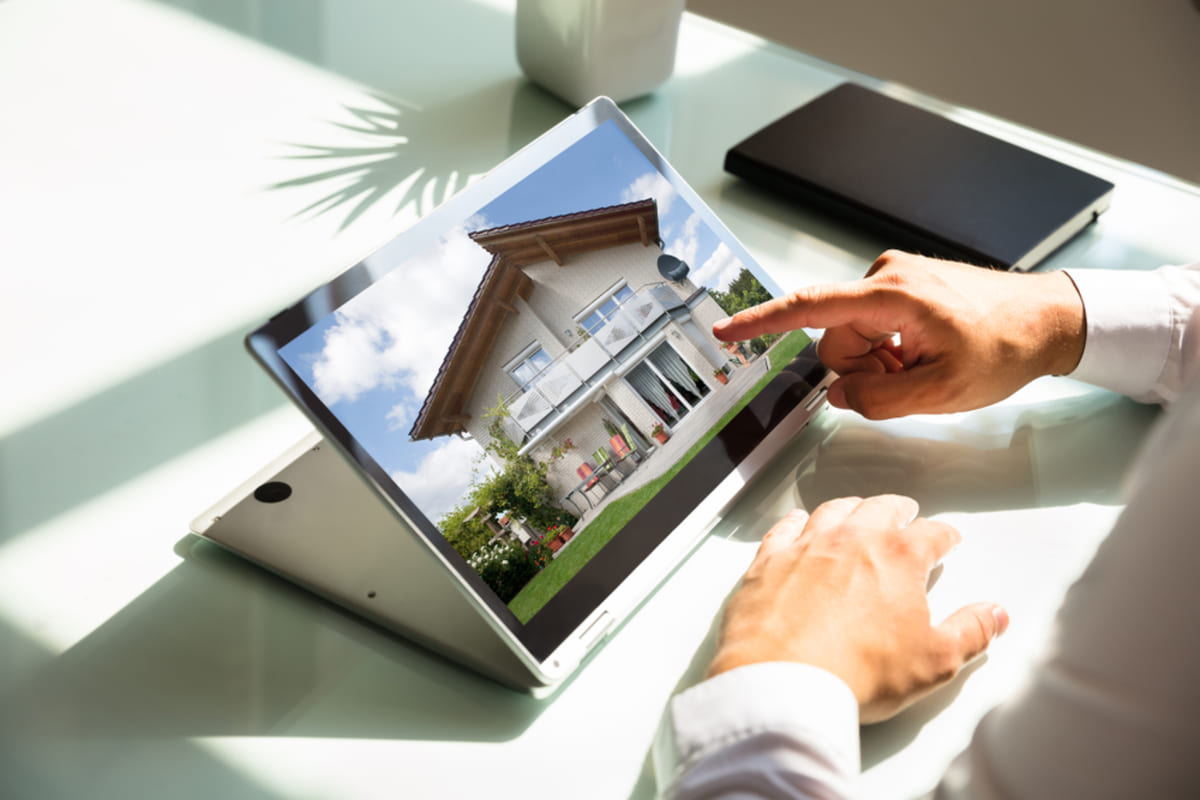 Close-up of businessman's hand looking at a house on a laptop, listing an Indianapolis rental property concept.