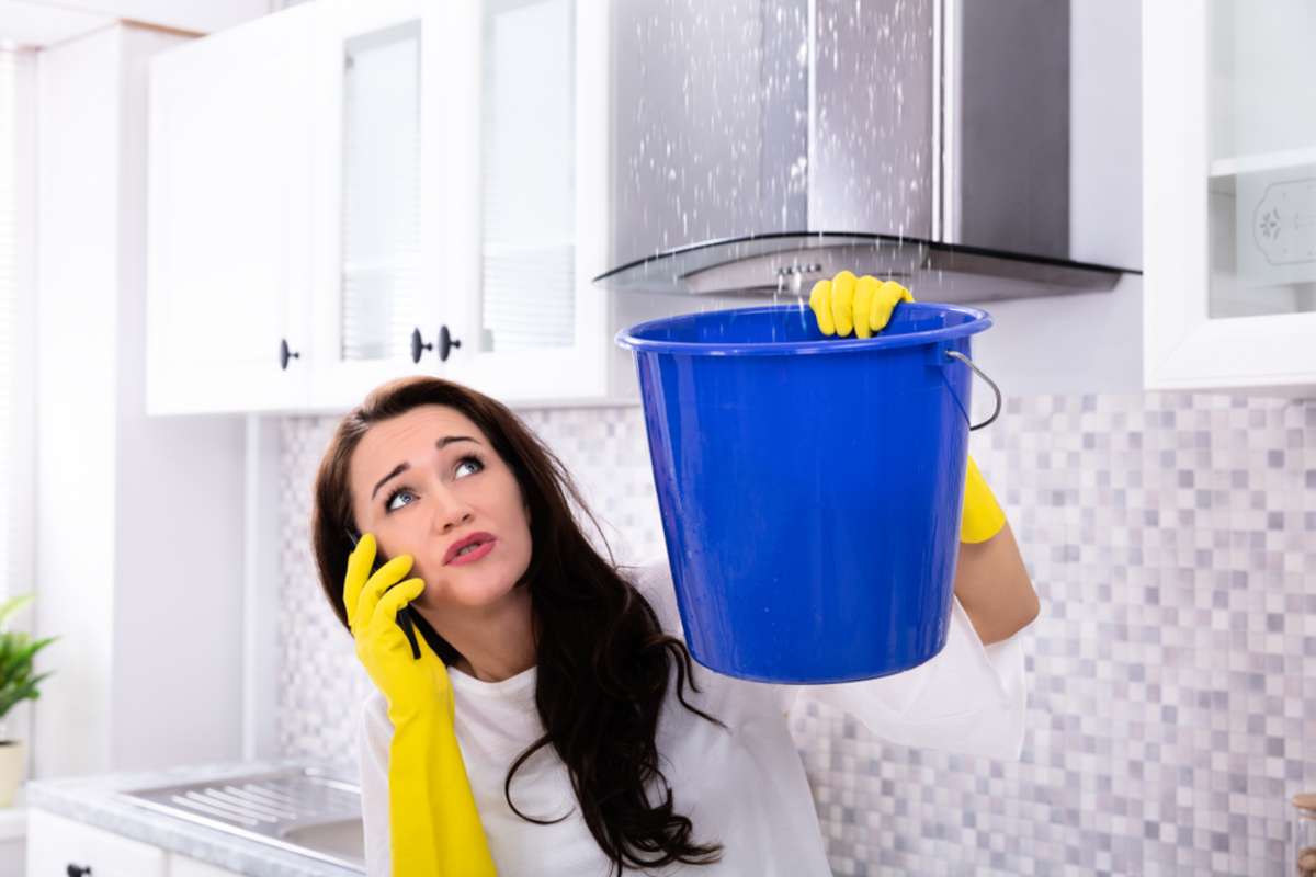 Woman holding bucket and calling about a roof leak, emergency maintenance concept